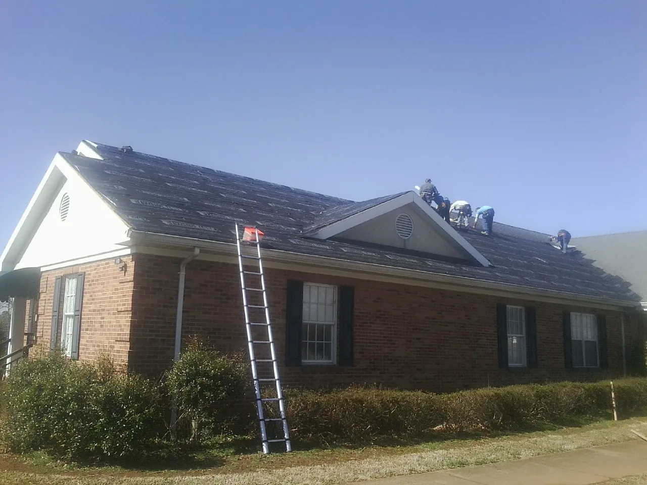 Crew tearing shingles off a brick ranch roof with a ladder set — Metal Roof Repair work by our crew in Bay Minette