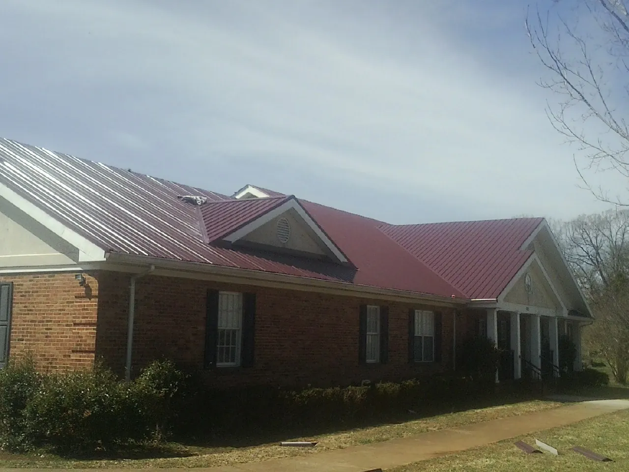Red metal roof with gabled entries on a long brick building, from a Hail Damage Roof Repair job in Bay Minette