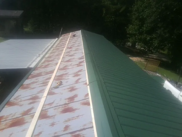 Old rusted panels beside newly installed green metal roofing — Wind Damage Roof Repair by Roofing Brothers in Bay Minette