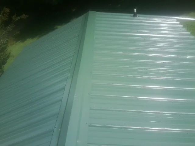 New green metal panels meeting at the ridge of a roof — Flat Roof Repair work by our crew in Bay Minette