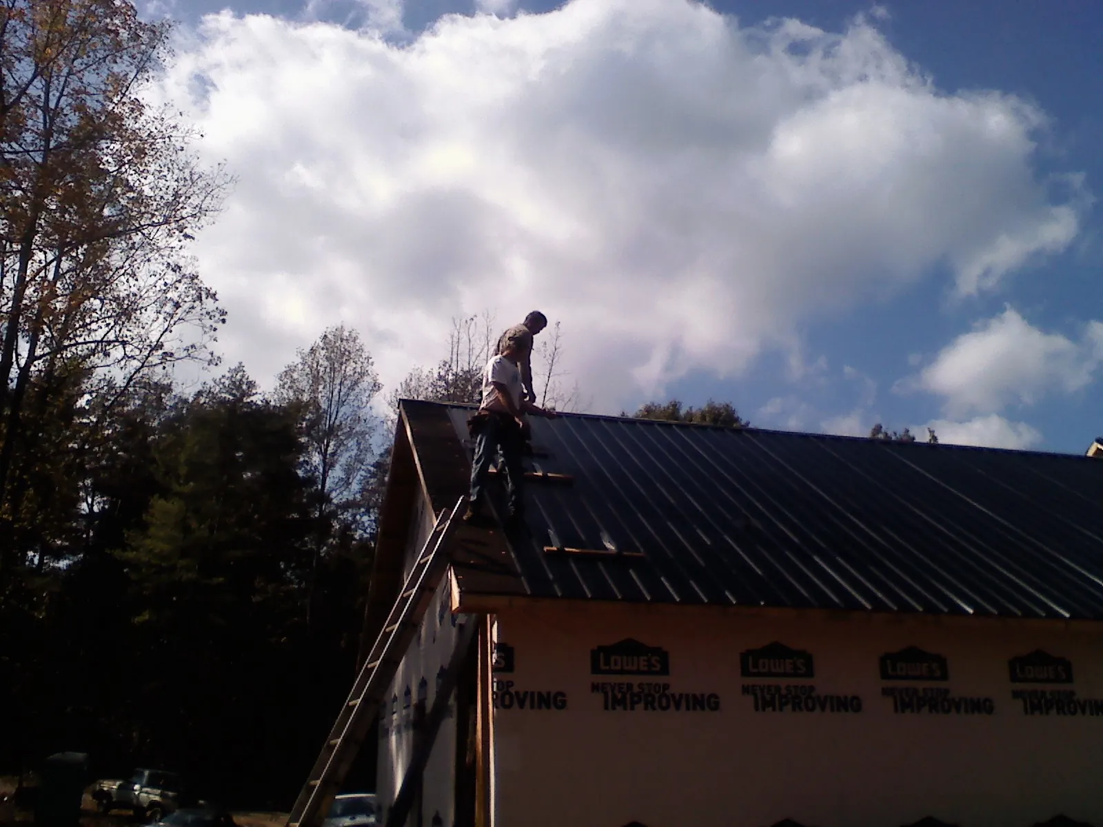 Roofer fastening dark metal panels high against a cloudy sky, from a Roof Inspection job in Bay Minette
