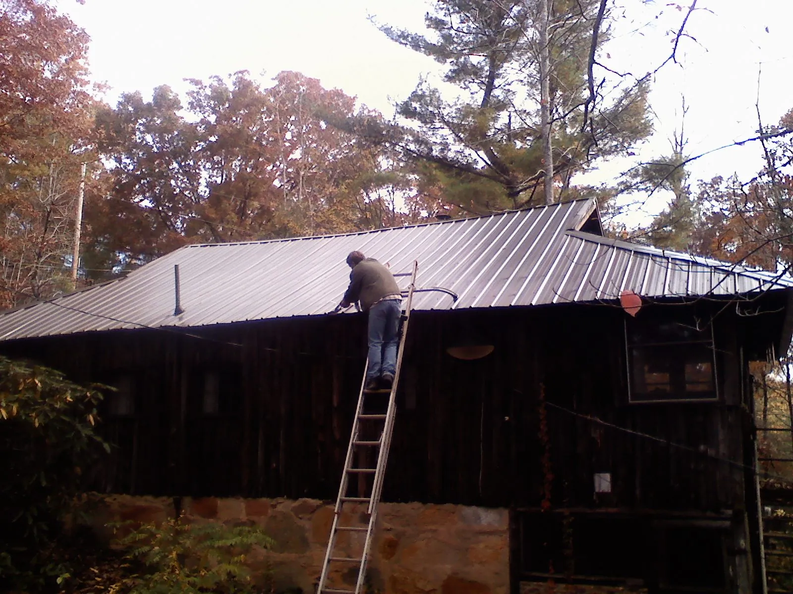 Roofer on a ladder working along the edge of a cabin metal roof in Bay Minette