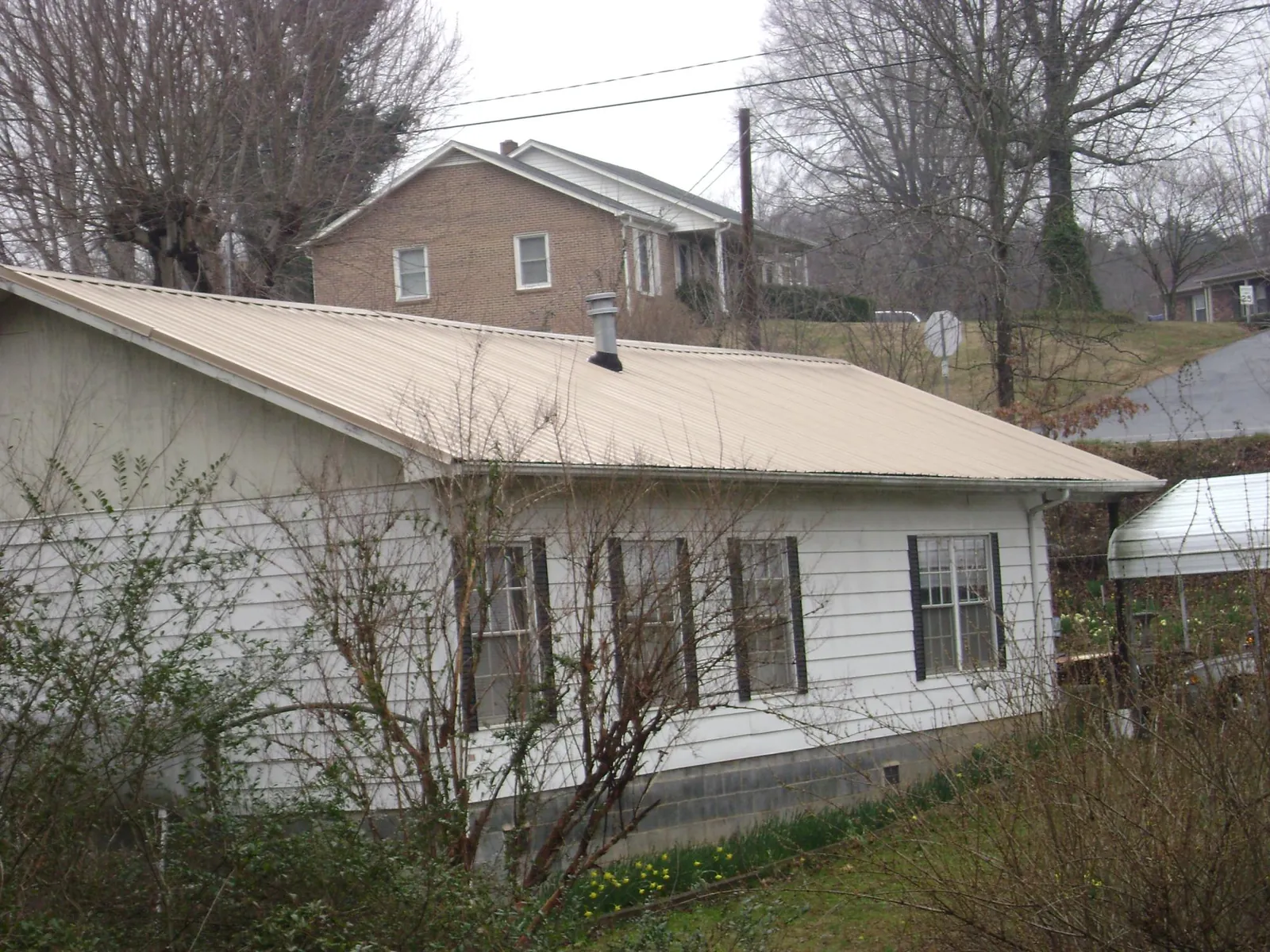 Tan metal roof on a white sided house set into a hillside — Commercial Roofing by Roofing Brothers in Bay Minette