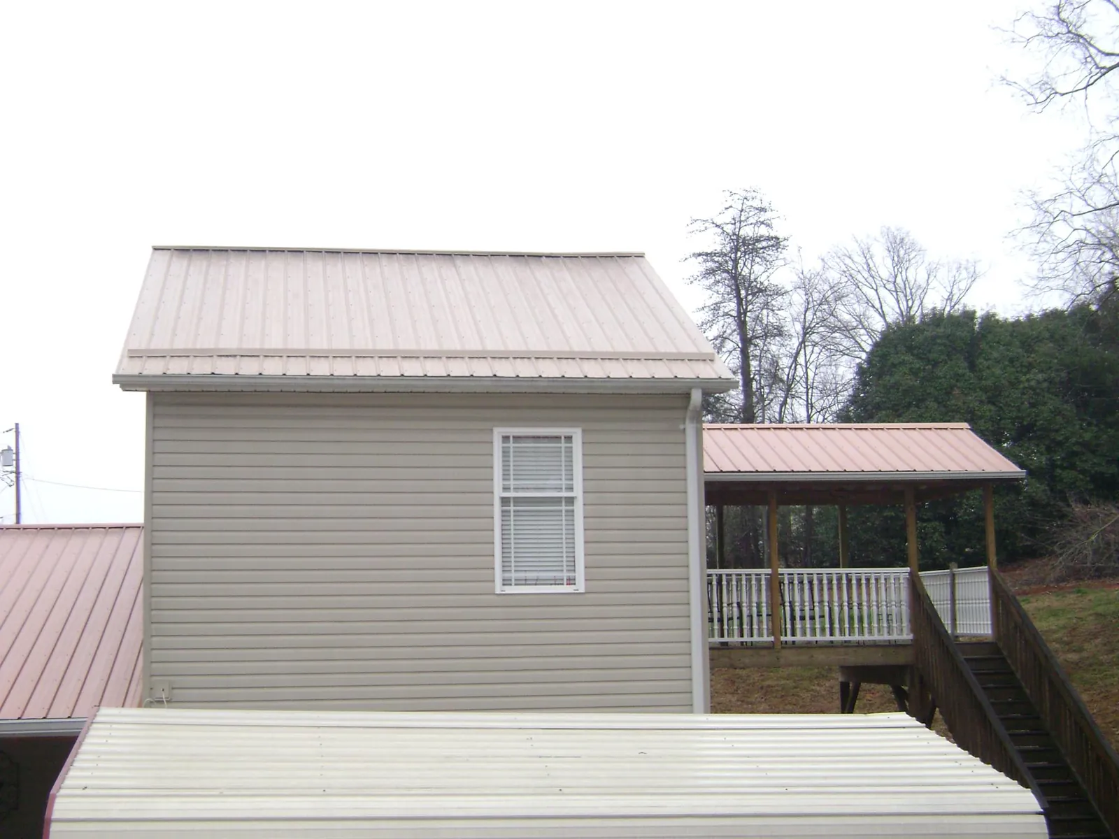 Tan metal roofs on a two story addition and attached porch, from a Roof Replacement job in Bay Minette